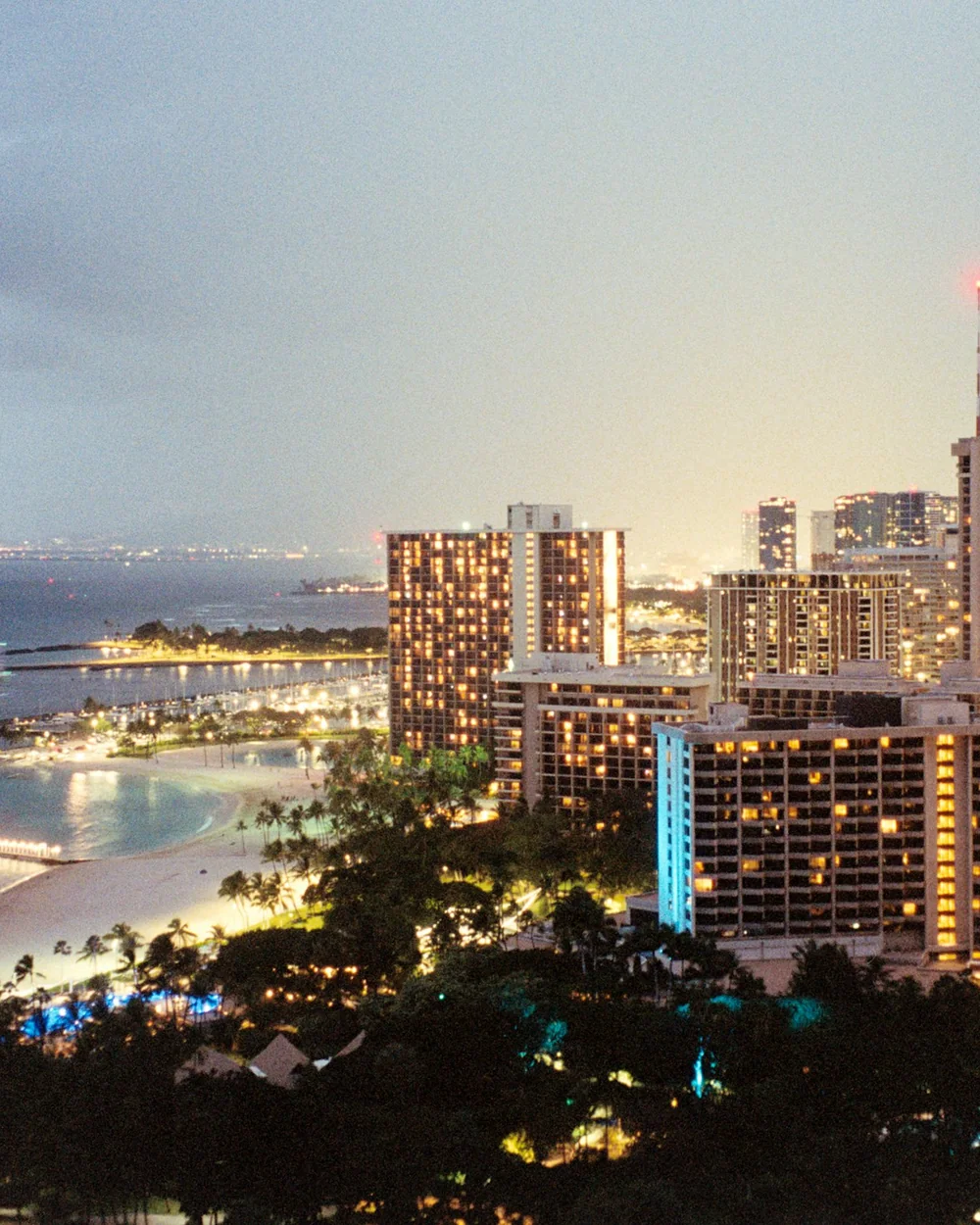 Panorama nábřeží Honolulu rozzářené za soumraku, viděné přes vodu z pláže (reprezentativní fotografie Honolulu za soumraku, nikoli vlastní trávník Ka Moana)